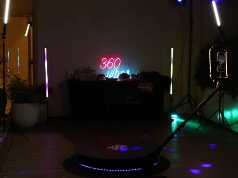360 photo booth platform with overhead camera arm and LED light tubes at a nighttime event